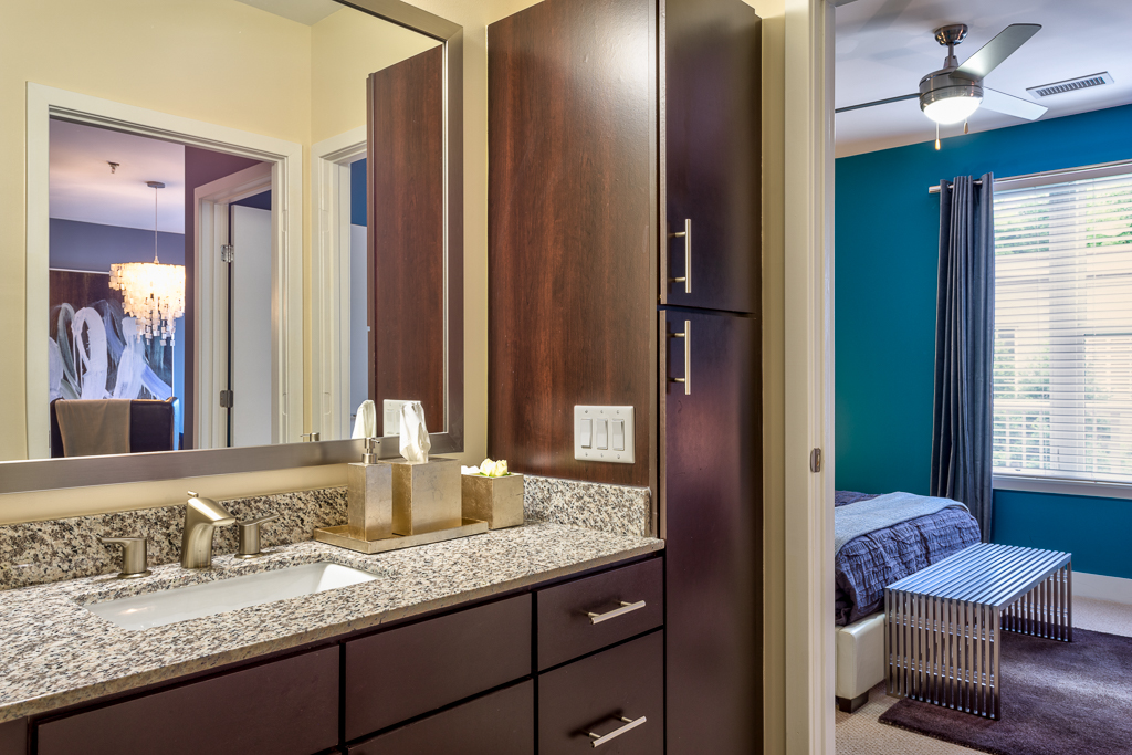 Bathroom area with granite countertops, single mirror, and access to bedroom