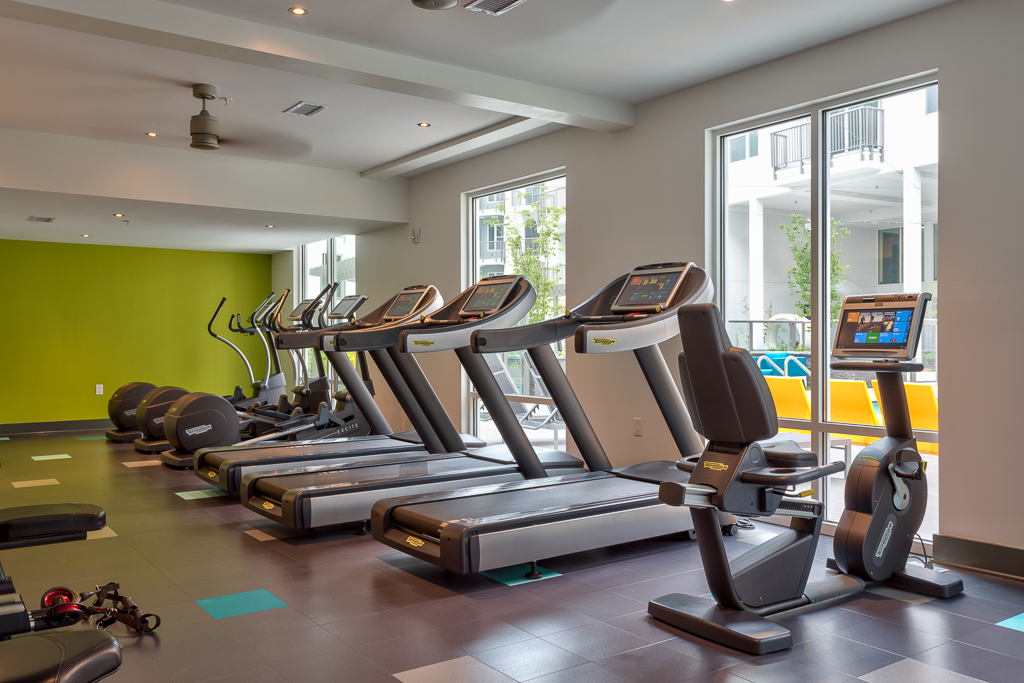 Indoor gym area with cardio machines and windows to outdoor pool